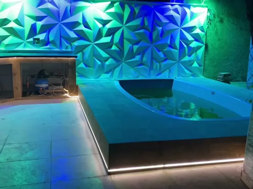 Área de lazer com piscina iluminada e parede com revestimento 3D